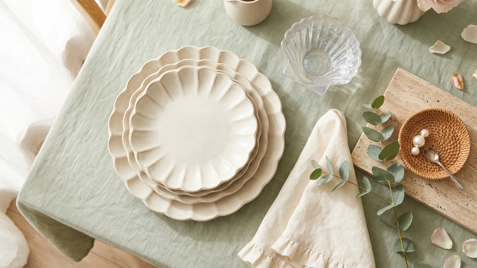 Illustration of scalloped-edge stoneware plates, a travertine tray and a rattan catchall on a cream table